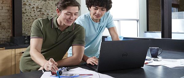 Two male college students casual clothing, leaning on a counter in an open study area with a Dell Inspiron 15 5000 Series (Model 5555) Non-Touch 15-inch notebook computer. A model car and sketches can be seen on the counter around them.